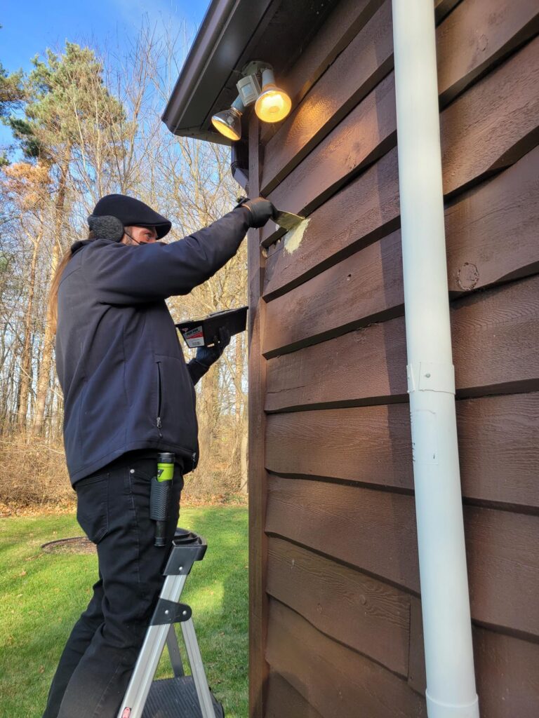 One of our technicians applying treatment on siding, representing one of our pest control services.