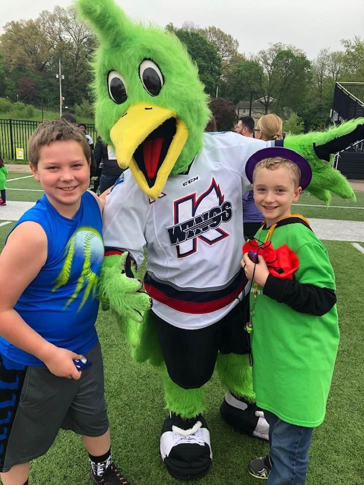The Kalamazoo Wings mascot and two children at a baseball game, representing the community connections of Pest Pros of Michigan.